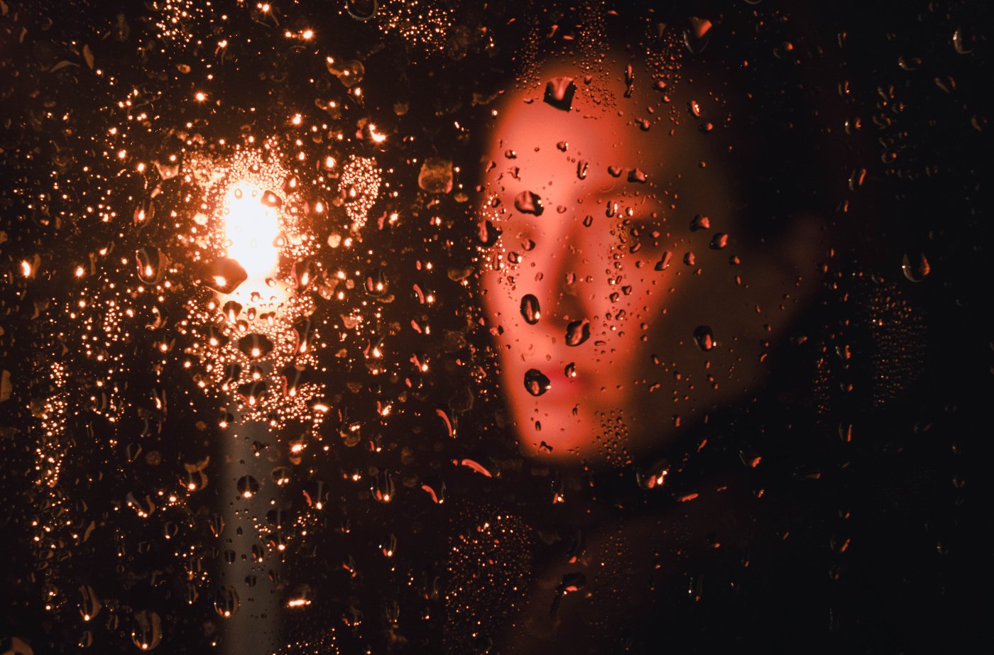 Face behind rain-streaked glass by candlelight